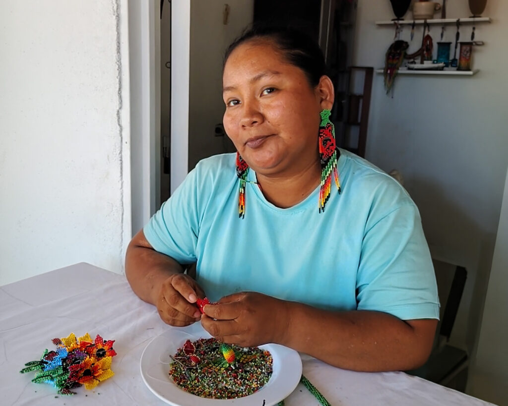 Artesana indígena del Amazonas colombiano tejiendo aretes de mostacilla hechos a mano con diseño de flores y colores tradicionales