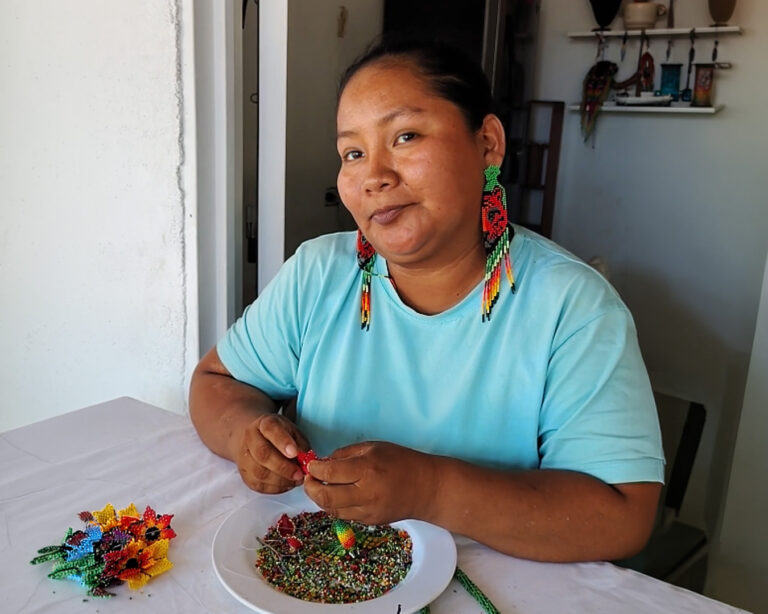 Artesana indígena del Amazonas colombiano tejiendo aretes de mostacilla hechos a mano con diseño de flores y colores tradicionales