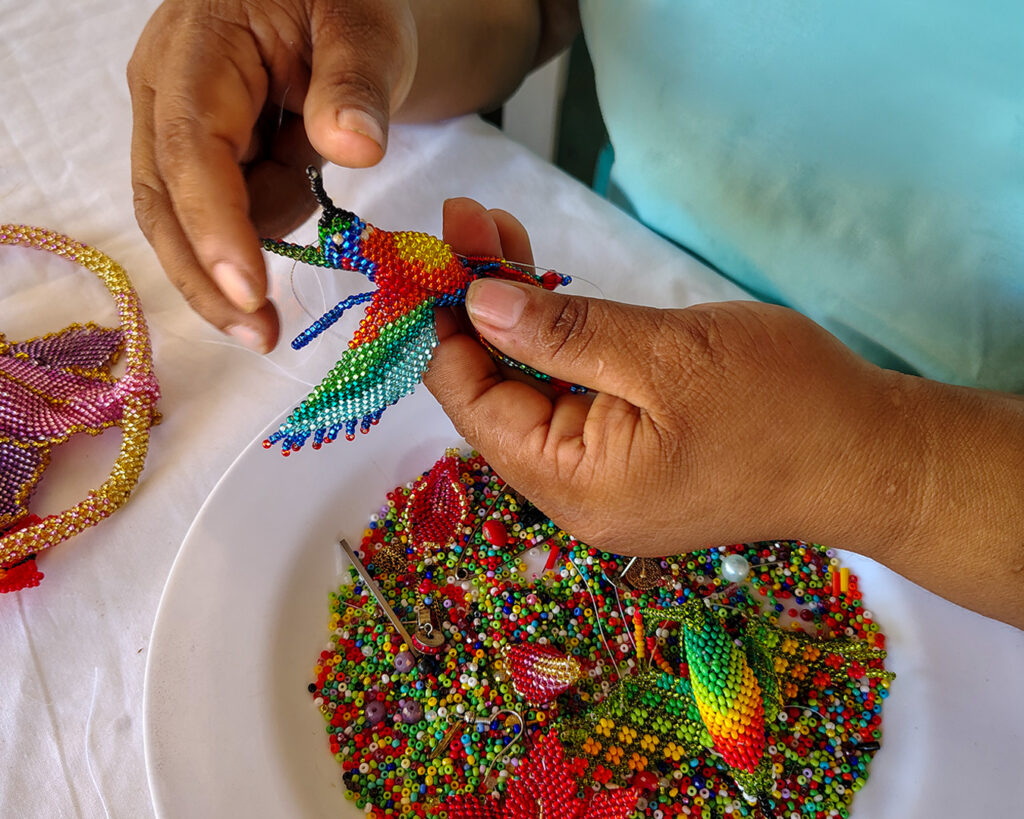 Artesana indígena del Amazonas colombiano tejiendo aretes de mostacilla hechos a mano con diseño de flores y colores tradicionales