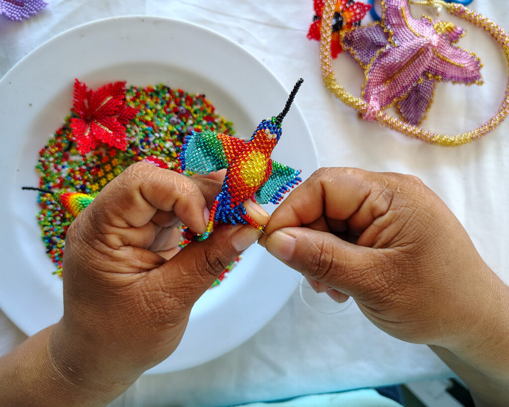 Artesana indígena del Amazonas colombiano tejiendo aretes de mostacilla hechos a mano con diseño de flores y colores tradicionales